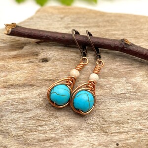 May include: A pair of turquoise and copper wire wrapped earrings with white beads. The earrings are hanging from a branch.
