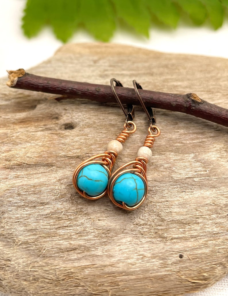 May include: A pair of turquoise and copper wire wrapped earrings with white beads. The earrings are hanging from a branch.
