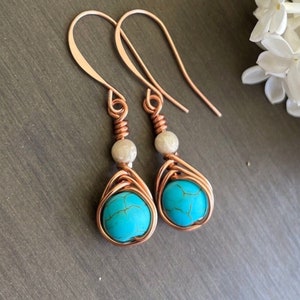 May include: A pair of copper wire wrapped earrings with turquoise stones and white pearl accents.