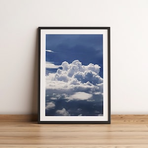 Peut inclure: Une photographie encadrée d'une grande formation de nuages ​​cumulus blancs sur un ciel bleu. Les nuages ​​sont moelleux et semblent éclairés d'en haut, créant un contraste saisissant.