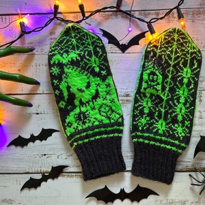 May include: A pair of black and green knitted mittens with a Halloween-themed design. The mittens feature bats, spiders, and a spooky tree pattern.
