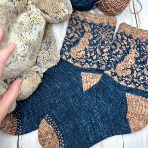 以下が含まれることがあります： 青と茶色のカラーリングで手編みされたソックスのペア。幾何学模様が施され、柔らかな糸で編まれています。