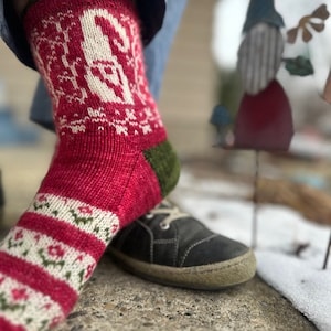 Può includere: Calze di lana rosse e bianche con tallone e punta verdi. Le calze presentano un motivo a fiocco di neve bianco.