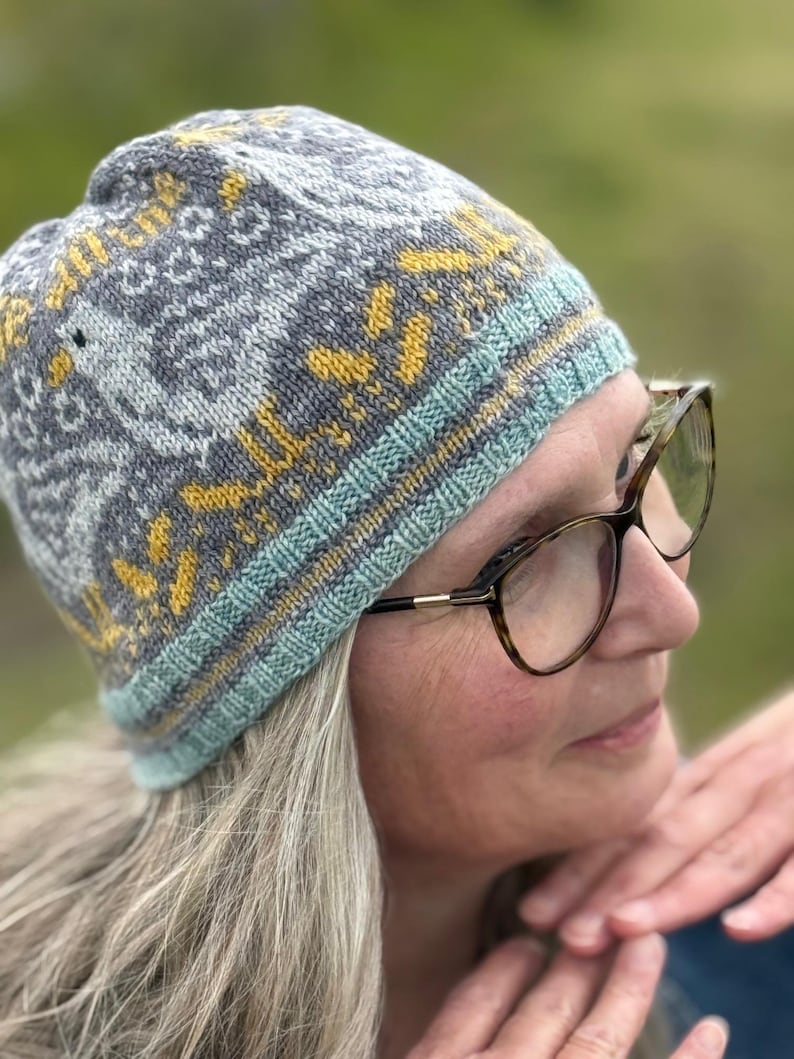 Puede incluir: Un gorro de punto gris con un patr&oacute;n geom&eacute;trico en amarillo y azul claro. El gorro tiene un borde acanalado en azul claro y amarillo. El gorro lo lleva una persona con gafas.