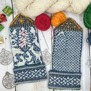 Könnte beinhalten: Ein Paar handgestrickte Fäustlinge mit Wintermotiv. Die Fäustlinge sind hauptsächlich blau und weiß und weisen ein Baum- und Schneeflockenmuster auf. Die Bündchen haben ein geometrisches Muster mit gelben Akzenten. Wolle und Stricknadeln befinden sich im Hintergrund.