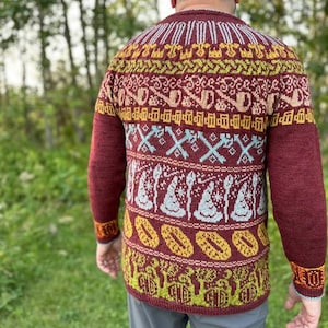 May include: A burgundy sweater with a detailed pattern in yellow, teal, and white. The design includes geometric shapes, stylized figures, and a repeating pattern of oval shapes. The sweater has long sleeves and a ribbed cuff.