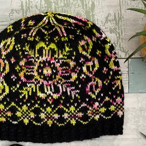 May include: A black knitted hat with a colourful geometric pattern in shades of pink, yellow, and white.