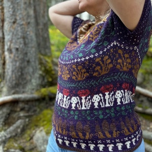 Pode incluir: Um su&eacute;ter de malha roxo, marrom e verde com um design de cogumelos e floresta. O su&eacute;ter tem mangas curtas e um decote em V.