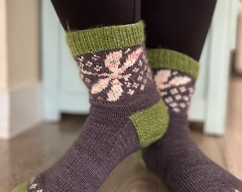 May include: A pair of dark gray socks with green and pink floral patterns. The socks are knitted and have a green cuff.