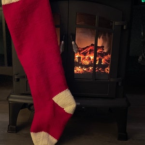 May include: A red and white knitted stocking hanging on a black fireplace with a glowing electric fireplace inside.