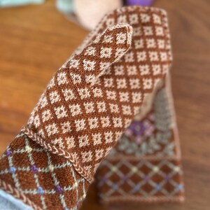 May include: A pair of brown and cream-colored knitted mittens with a diamond pattern. The mittens have a floral design on the cuff and are made of a soft, textured yarn. The cuff features a diamond pattern with small accents of purple and yellow.