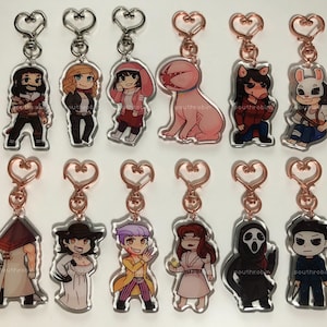 May include: Twelve different character keychains featuring various horror movie characters. Each keychain is made of clear acrylic and features a different character from a horror movie. The keychains are attached to a silver or rose gold heart-shaped ring.
