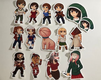 May include: A set of 14 colorful cartoon stickers featuring characters from various video games and movies. The stickers are printed on white paper and have a glossy finish. The characters include a pink creature, a pyramid-headed figure, a woman with a green hooded cloak, and a woman with a red dress.