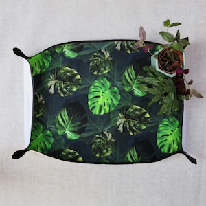 May include: A black and green patterned throw pillow with a dark background and a black border. The pillow features a repeating pattern of large green leaves.