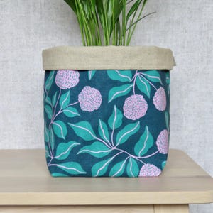 May include: A teal fabric planter with a pink floral pattern. The planter has a linen top and is filled with a green plant.