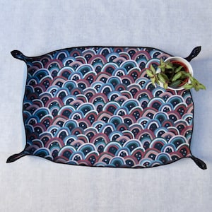 May include: A black tray with a colourful, abstract pattern of overlapping arches in shades of blue, pink, and white. The tray has a black border and a slightly rounded shape.