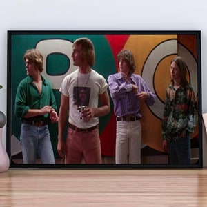 May include: A framed print featuring four people in vintage clothing, standing in front of a colorful backdrop. The print is in a black frame and is displayed on a wooden surface. The image has a retro aesthetic.