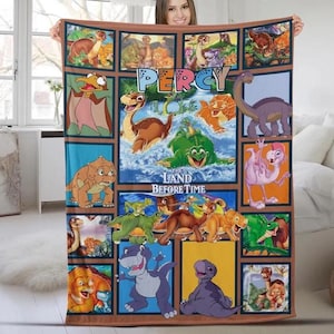 May include: A colorful blanket featuring cartoon dinosaurs from "The Land Before Time" movie. The blanket has a grid design with various dinosaur illustrations, the word "PERCY", and the movie title. The color palette includes blues, greens, browns, and oranges.