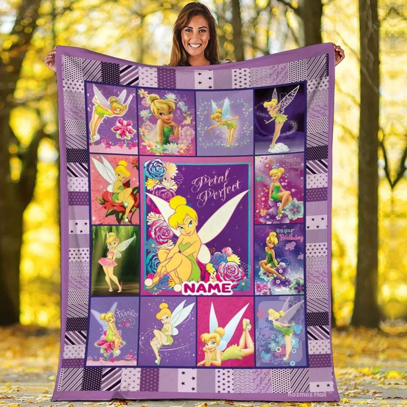K&ouml;nnte beinhalten: Eine lila-wei&szlig;e Steppdecke mit Bildern von Tinkerbell. Die Steppdecke hat ein Patchwork-Design mit verschiedenen Bildern der Fee, zusammen mit den Worten "Petal Perfect" und einem Platz f&uuml;r einen Namen. Die Decke wird von einer Person gehalten.