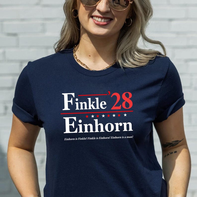 May include: Navy blue t-shirt with the text "Finkle '28 Einhorn" in white and red. The design includes five stars and the phrase "Einhorn is Finkle! Finkle is Einhorn! Einhorn is a man!"