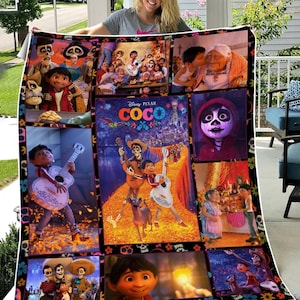 May include: A colorful blanket featuring scenes and characters from the Disney Pixar movie "Coco." The blanket displays multiple images, including the movie title, characters playing guitars, and scenes with skeletons and family members. The border is decorated with floral and skull motifs.