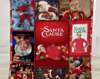 May include: A red and white Christmas-themed blanket featuring images from the movie "The Santa Clause." The blanket displays various scenes and the movie title in white lettering against a red background. The blanket is held up by a person.