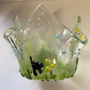 Op de afbeelding: Een glazen kaarsenhouder met een groen en geel ontwerp. De houder heeft een zwarte kat en gele bloemen.