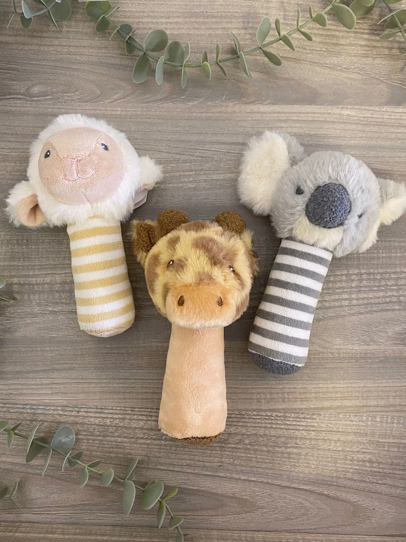 May include: Three plush baby toys with rattle handles. The toys are a white lamb, a brown giraffe, and a gray koala.