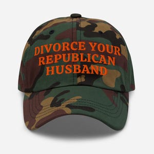 Könnte beinhalten: Eine Camouflage-Baseballkappe mit dem Text "DIVORCE YOUR REPUBLICAN HUSBAND" in Orange gestickt. Die Kappe hat einen gebogenen Schirm und einen schwarzen Knopf. Hergestellt aus strapazierfähigem Stoff.