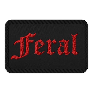 Könnte beinhalten: Schwarzer rechteckiger Aufnäher mit dem roten Wort "Feral" in gotischer Schrift gestickt. Der Aufnäher hat einen schwarzen Rand und ist zum Aufnähen oder Aufbügeln auf Kleidung oder Accessoires bestimmt.