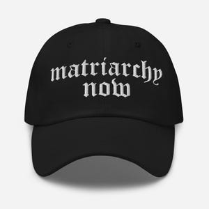 Puede incluir: Gorra de béisbol negra con el texto blanco bordado "matriarchy now". La gorra tiene una visera curva y un botón en la parte superior. Un accesorio casual.