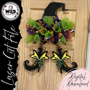 May include: A Halloween-themed door decoration featuring a black witch hat and legs. The hat is adorned with a purple band and a decorative mesh wreath in green, orange, and purple. The witch's legs and shoes are black with yellow bows and green accents. The text "Laser Cut File" is on the left.