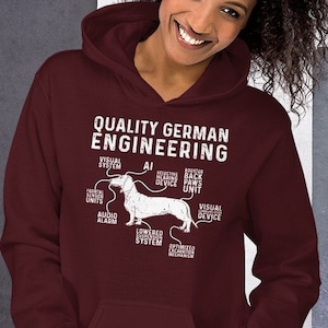 May include: A maroon hoodie with the text "QUALITY GERMAN ENGINEERING" and a diagram of a dachshund. The diagram includes labels such as "VISUAL SYSTEM" and "AUDIO ALARM". The hoodie has a front pocket and a hood.
