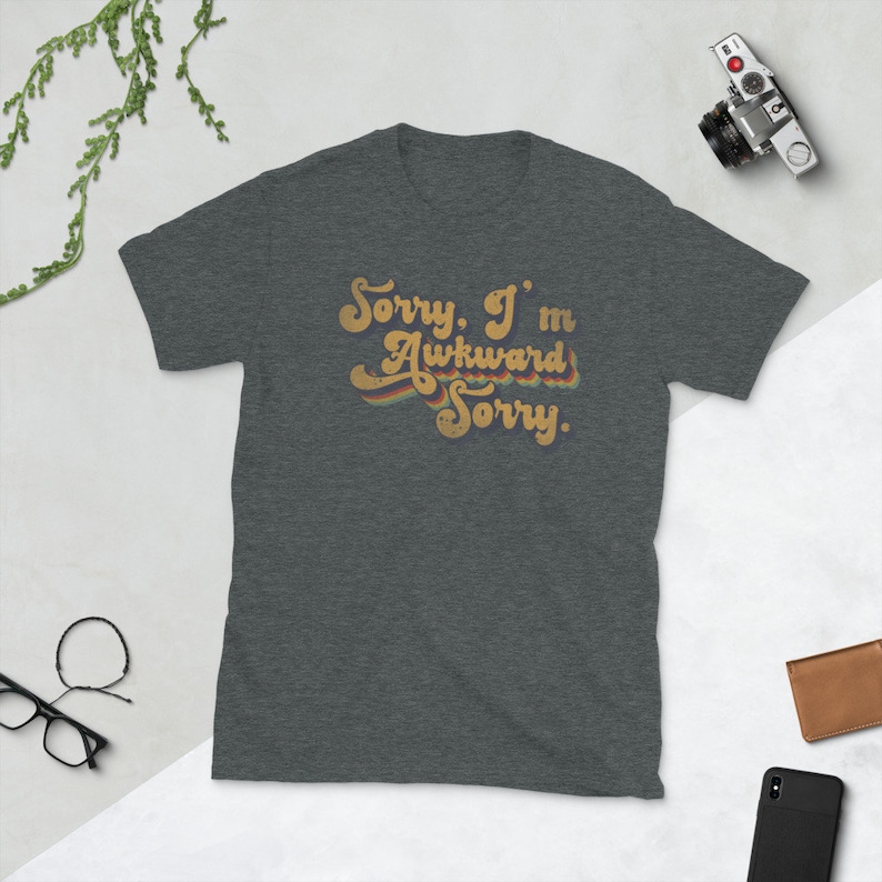 Puede incluir: Una camiseta gris oscuro jaspeada con un gr&aacute;fico de estilo retro que dice "Lo siento. Soy torpe Lo siento."