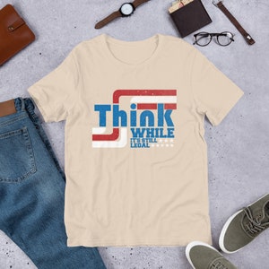 May include: A beige t-shirt with a red, white, and blue graphic that says "Think While It's Still Legal" with stars.