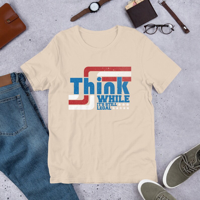 May include: A beige t-shirt with a red, white, and blue graphic that says "Think While It's Still Legal" with stars.