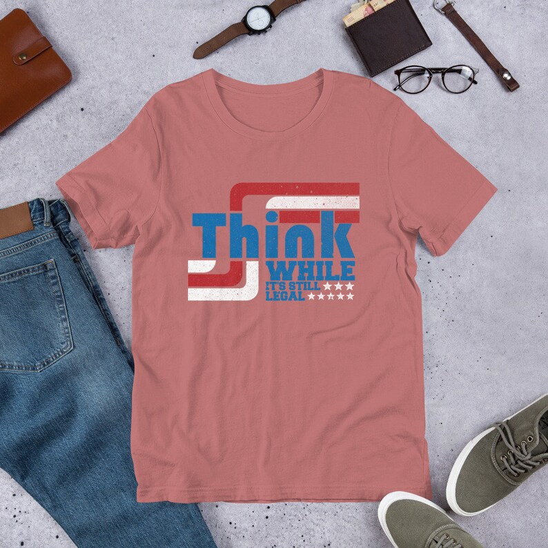 May include: A pink t-shirt with a distressed American flag design and the text "Think While It's Still Legal" in blue and white.