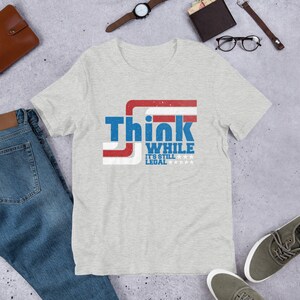 May include: A heather grey t-shirt with a red, white, and blue graphic that says "Think While It's Still Legal" with stars.