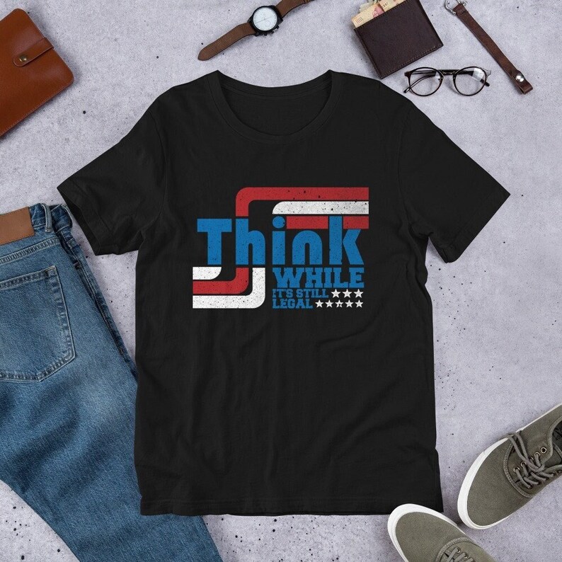 May include: Black t-shirt with a red, white, and blue American flag design. The text "Think While It's Still Legal" is printed on the shirt.