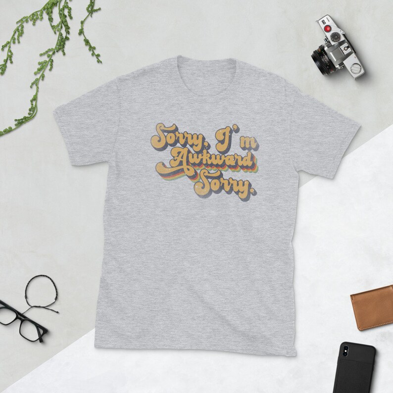 Puede incluir: Una camiseta gris jaspeada con un gr&aacute;fico de estilo retro que dice "Lo siento, soy torpe Lo siento."