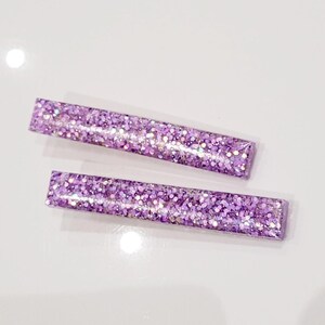 May include: Two purple glitter hair clips. The clips are rectangular and have a sparkly finish.