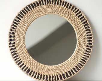 May include: Round woven mirror with a black and natural rattan frame. The mirror has a simple, modern design.