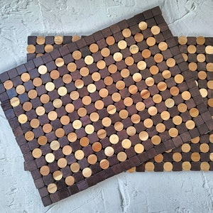 May include: Two wooden trivets with a geometric pattern of alternating dark brown squares and light brown circles. The trivets are made of small wooden pieces and are designed to protect surfaces from heat.