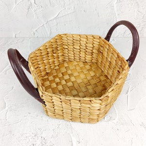 May include: A hexagonal woven basket with brown leather handles. The basket is made of natural materials and has a light brown color.