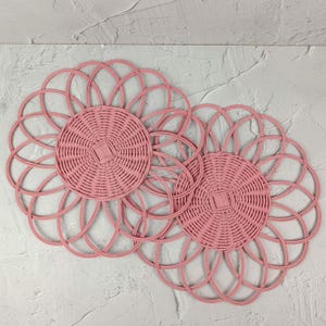 May include: Three pink woven wicker placemats with a circular design. The placemats are made of a woven material and have a delicate, feminine look.