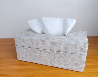 May include: A gray tissue box cover with a woven texture. The box is empty and the top is open, revealing a white tissue.