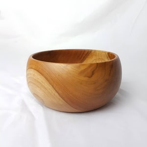 May include: A large, wooden bowl made from natural wood. The bowl has a smooth, rounded shape and a natural wood grain pattern.