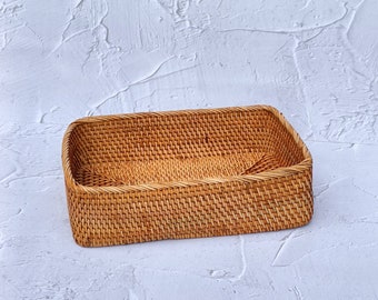 Puede incluir: Una cesta rectangular de mimbre tejida de color marrón natural. La cesta está vacía y tiene un tejido liso y uniforme.