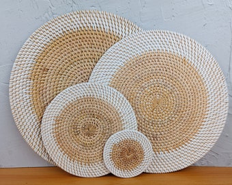 May include: Set of four round woven placemats in natural brown and white. The placemats are made of a natural material and have a unique, hand-woven design.