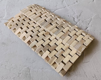 May include: A set of two natural wood woven mats. The mats are made of thin strips of wood that are woven together to create a grid pattern. The mats are light brown in color and have a natural, rustic look.